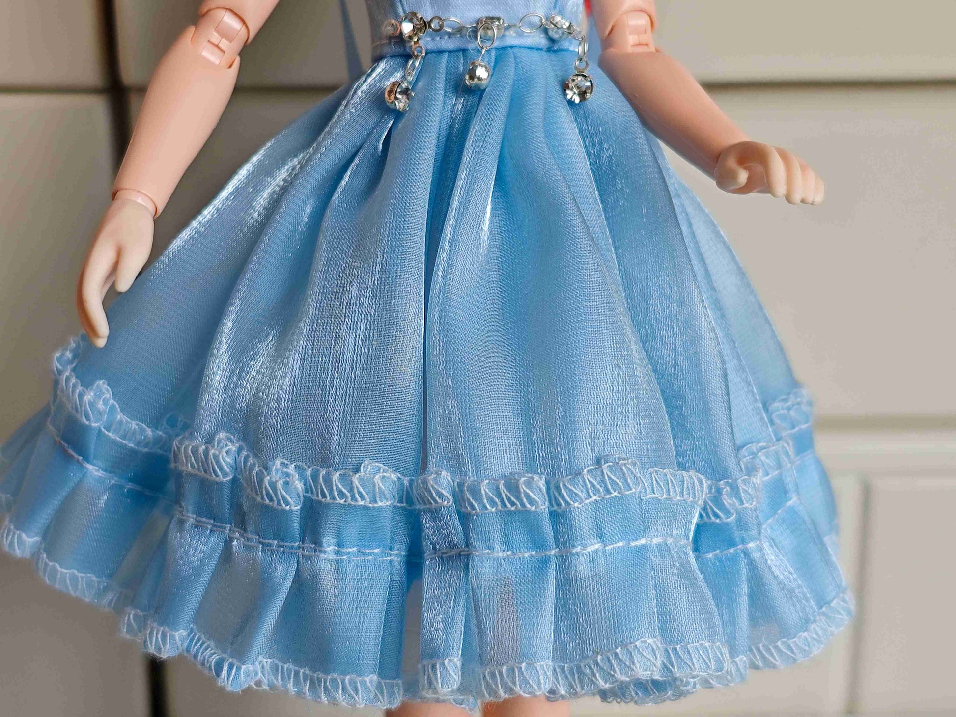 Detailed view of the sparkling ice blue fabric and textured fabric layers on the doll gown skirt.