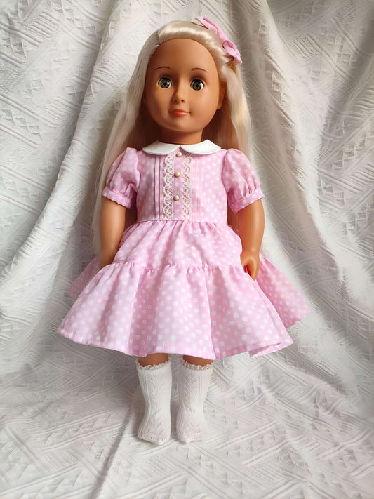 A sweet 18 inch doll wearing a handmade pink polka dot dress with a Peter Pan collar.
