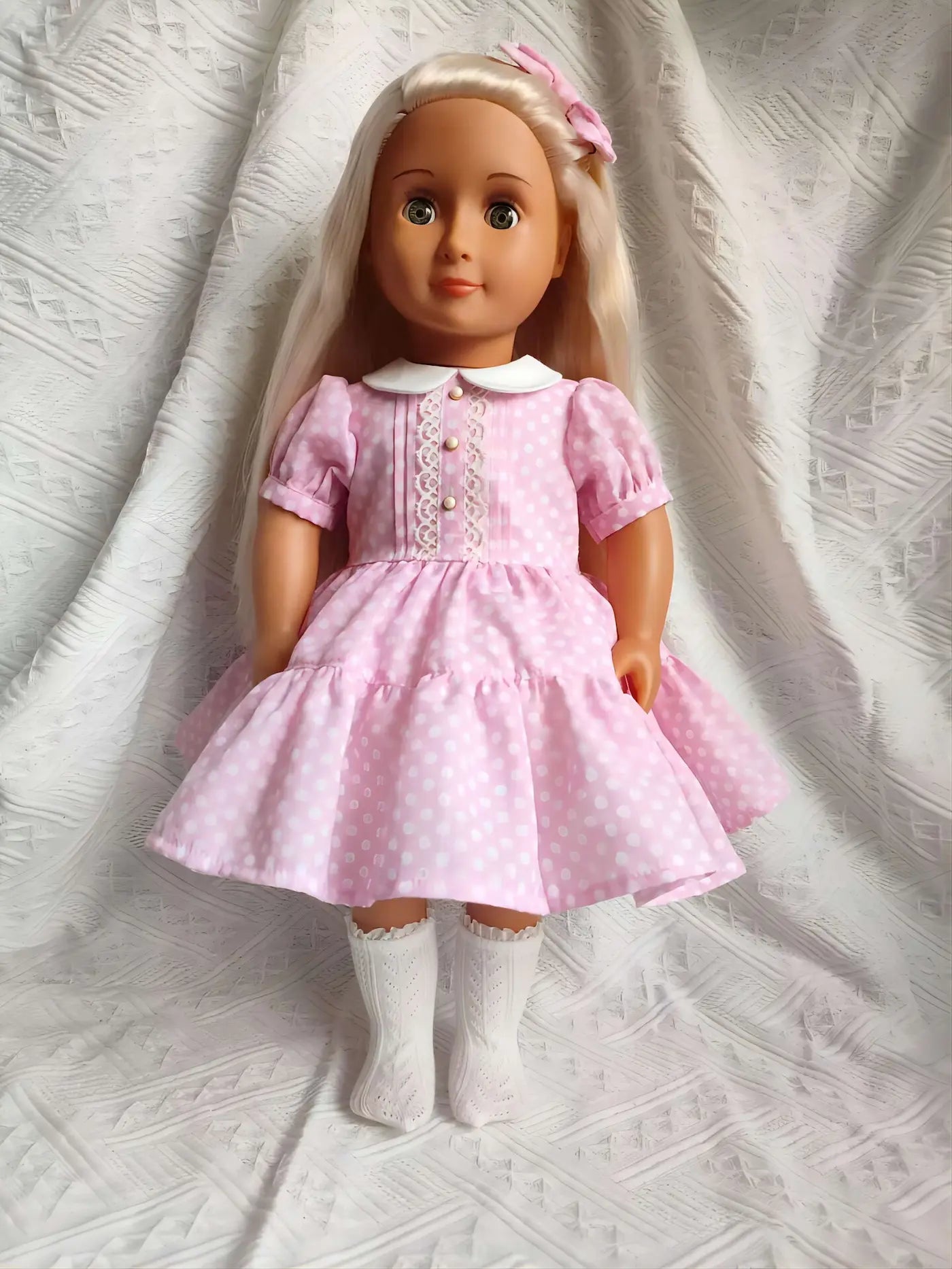 A sweet 18 inch doll wearing a handmade pink polka dot dress with a Peter Pan collar.