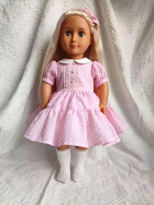 A sweet 18 inch doll wearing a handmade pink polka dot dress with a Peter Pan collar.