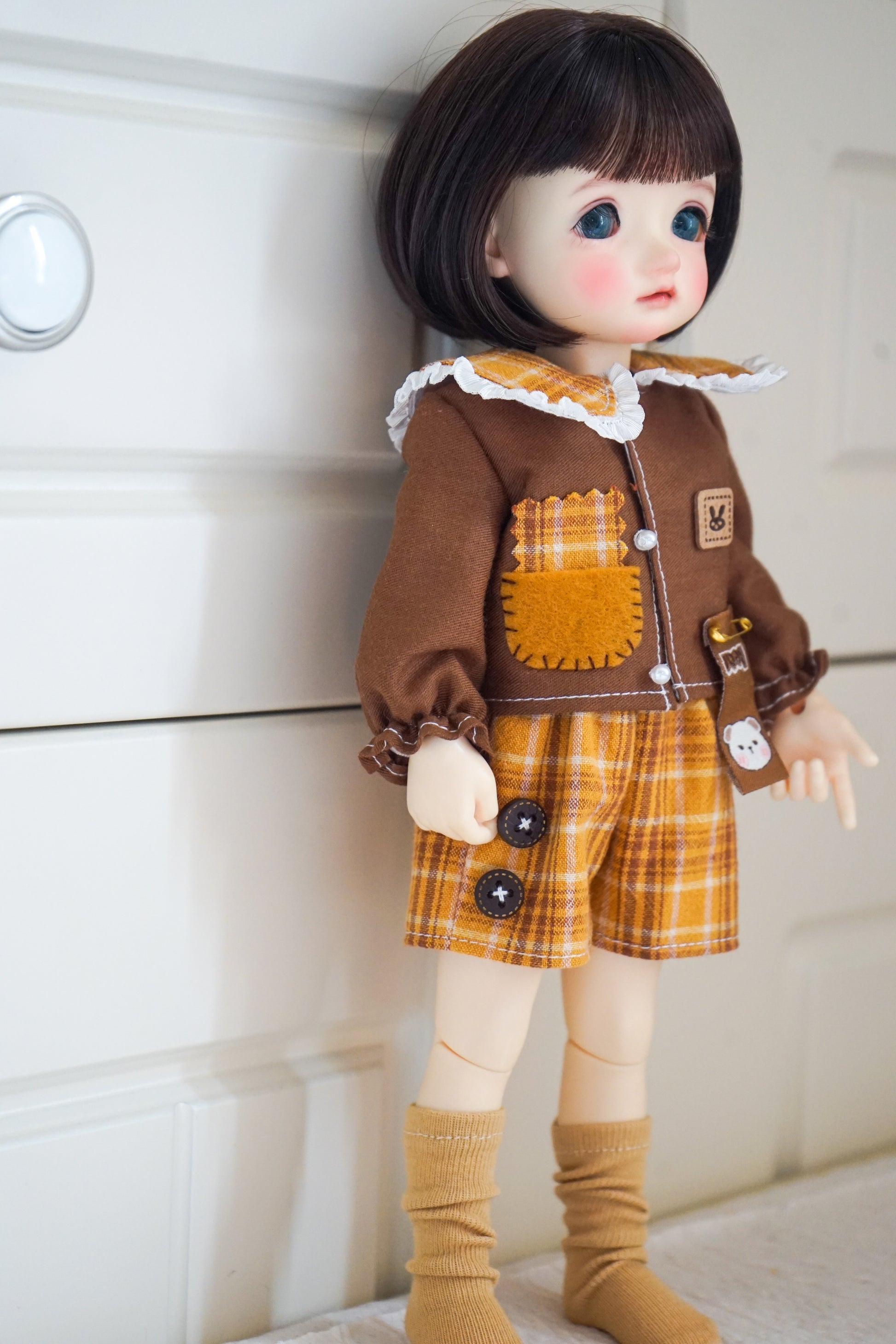 Side view of yellow cat patch shirt and plaid shorts on 1/6 BJD doll.